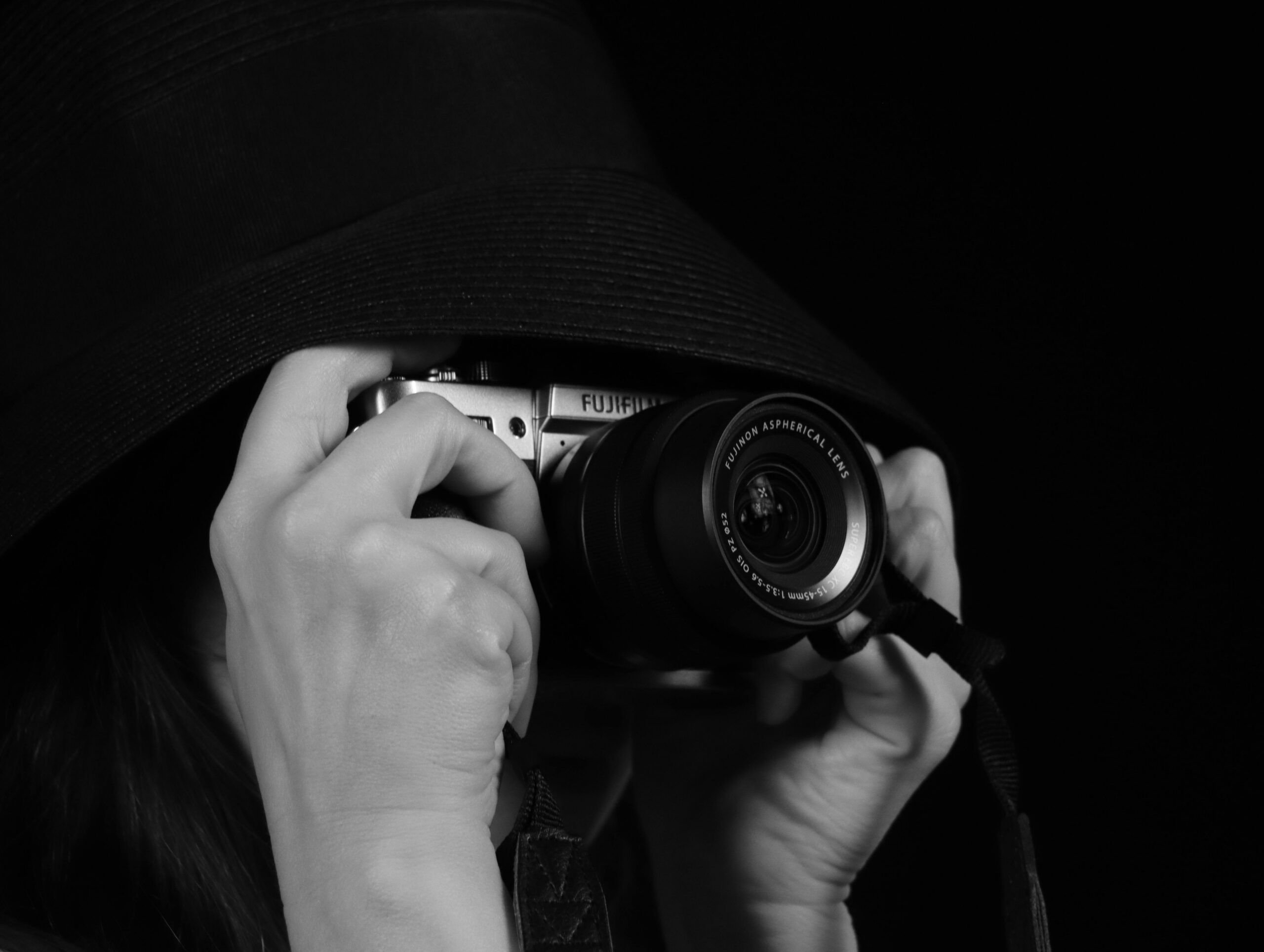 Services Black and white portrait of a person using a camera partially hidden by a hat.